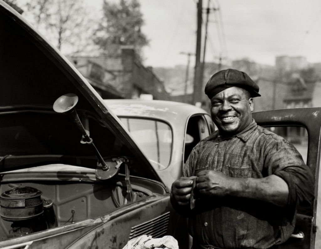 11. Auto mechanic Sam 'Scotty' Scott, standing next to the car with an open hood, 1941